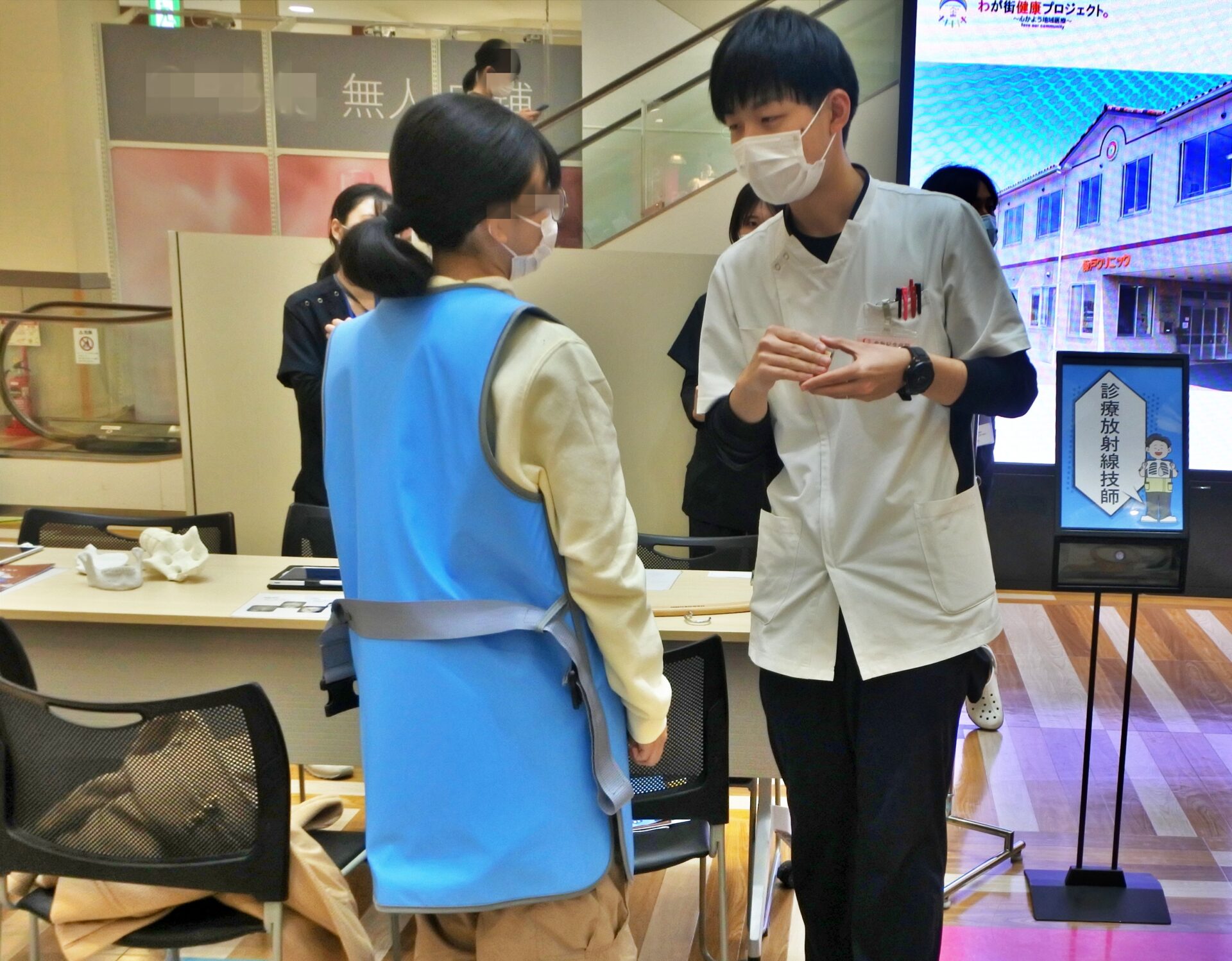 診療放射線技師ブースで、放射線防護衣を着る参加者