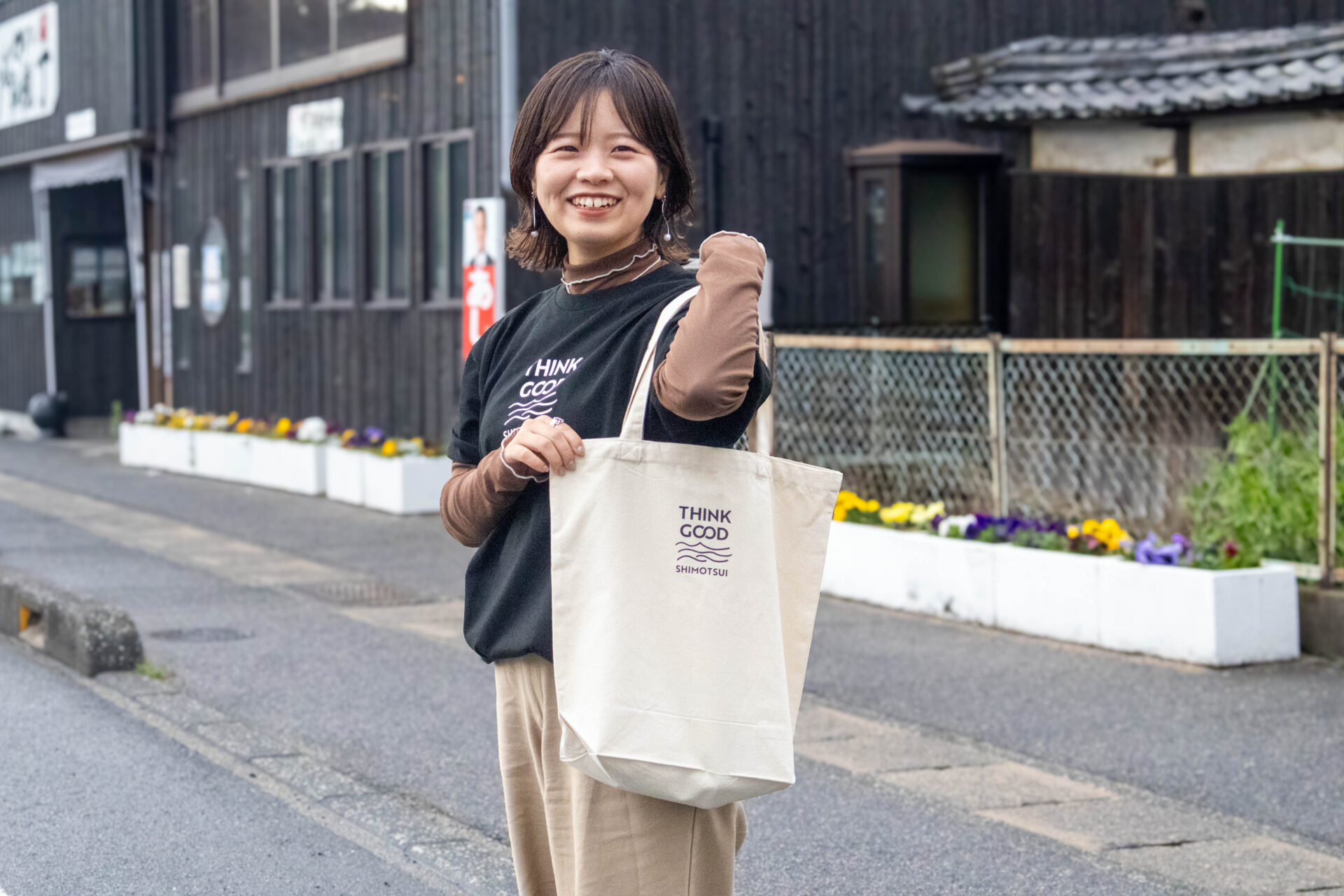 「THINK GOOD SHIMOTSUI」のTシャツとトートバッグを身につける中道さん